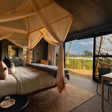 Luxury safari tent interior at North Island Okavango with canopy bed and panoramic delta views through floor-to-ceiling windows