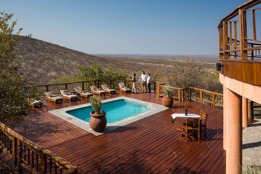 Transats disposés autour de la piscine sur la terrasse en bois de l'Etosha Mountain Lodge, avec les collines de dolomite en toile de fond.