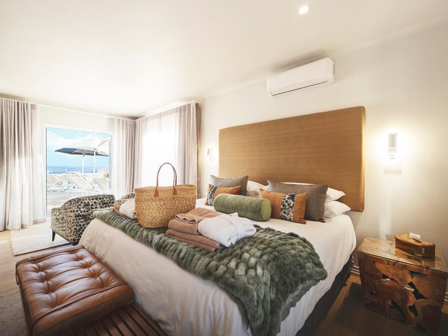 Luxuriöse Suite direkt am Strand mit Kingsize-Bett, Kopfteil aus Holz, kuscheligen Bettdecken und Blick auf die Berge durch große Fenster.