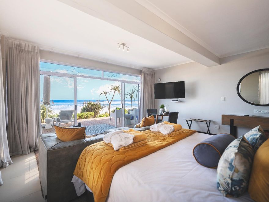 Luxuriöse Suite direkt am Strand mit Kingsize-Bett, Meerblick durch Panoramafenster, moderner Einrichtung und grauen Vorhängen in der Beach Villa Wilderness.
