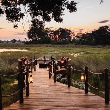 Wooden boardwalk with lanterns leading to Okavango Delta safari lodge at sunset across wetlands