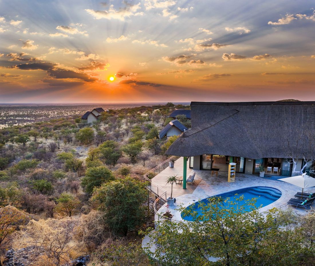 Le lodge principal au toit de chaume de Safarihoek et sa piscine au sommet de la colline, avec les chalets disséminés dans le bush en contrebas au coucher du soleil.