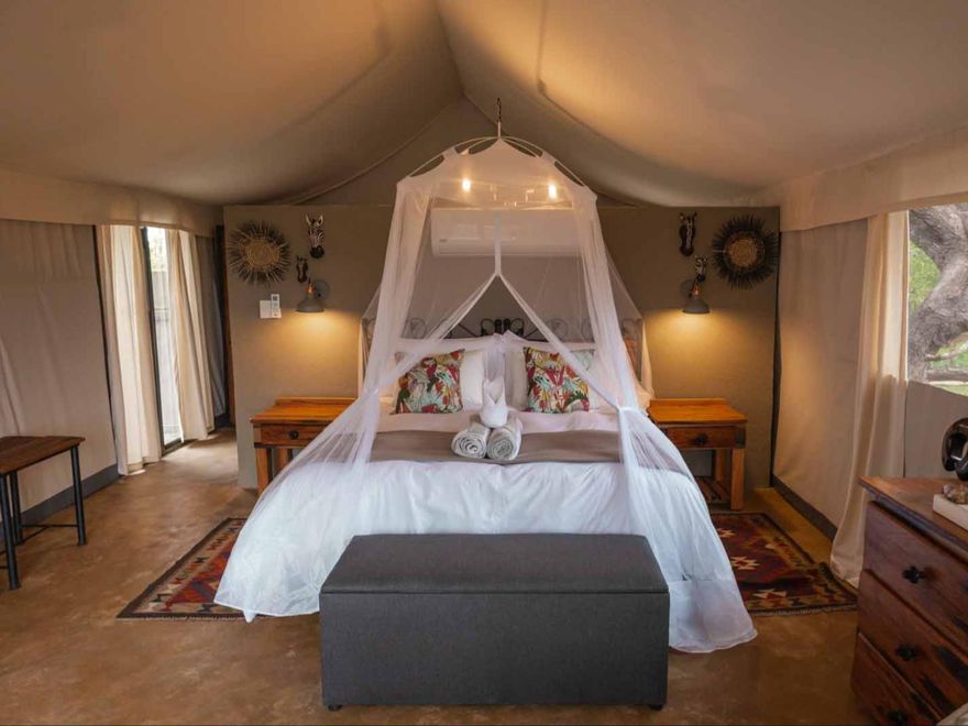 Interni di lusso della tenda safari con letto a baldacchino, cuscini colorati e arredamento rustico all'Umkumbe Bush Lodge