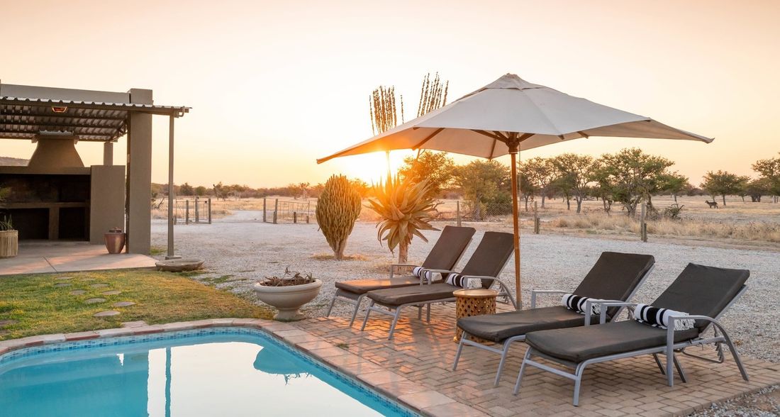Chaises longues et parasol au bord de la piscine privée de la Safari House, avec l'espace barbecue en arrière-plan.