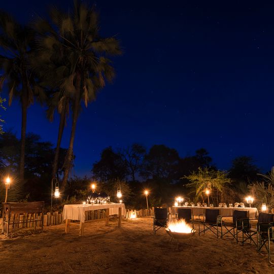 Abendlicher Spaziergang mit Laternen durch das Pelo Camp mit Palmen und Zeltunterkünften im Okavango-Delta