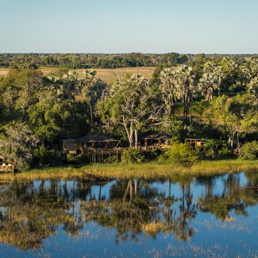Luxuriöse Safarizelte mit Blick auf die ruhige Lagune im Pelo Camp im Okavango-Delta, wo sich die Bäume im stillen Wasser spiegeln.